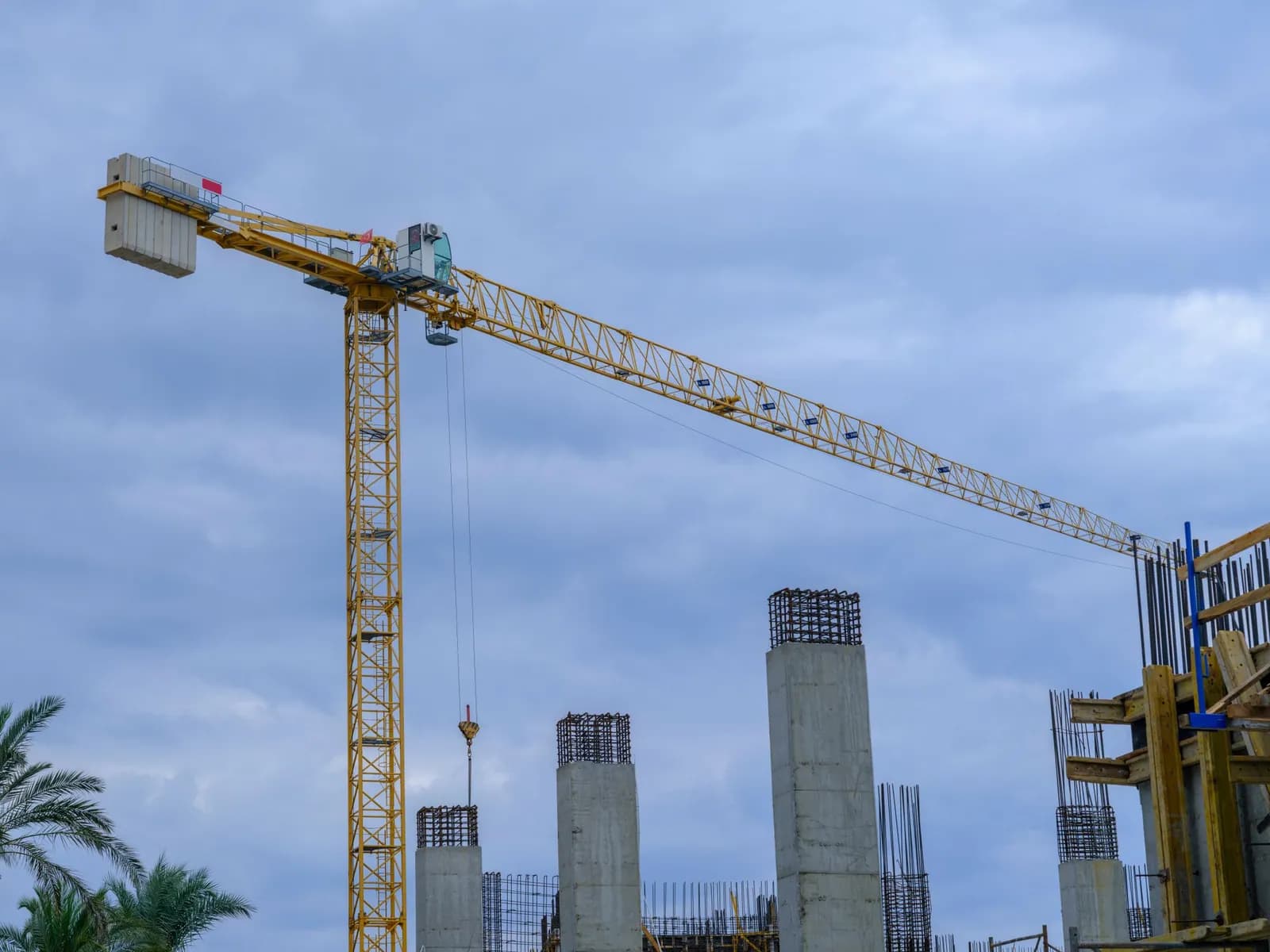 Gelber Turmdrehkran über einem Rohbau mit Betonstützen vor bewölktem Himmel