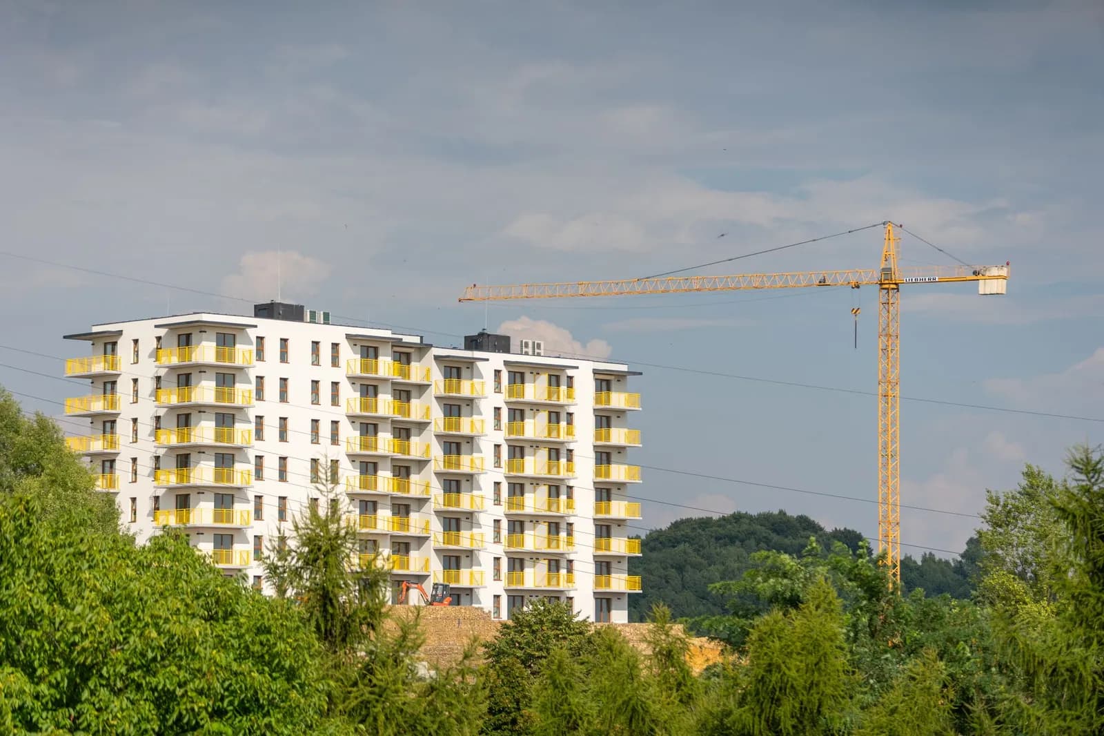 Mehrfamilienhaus im Rohbau mit Baukran neben fertigen Wohngebäuden