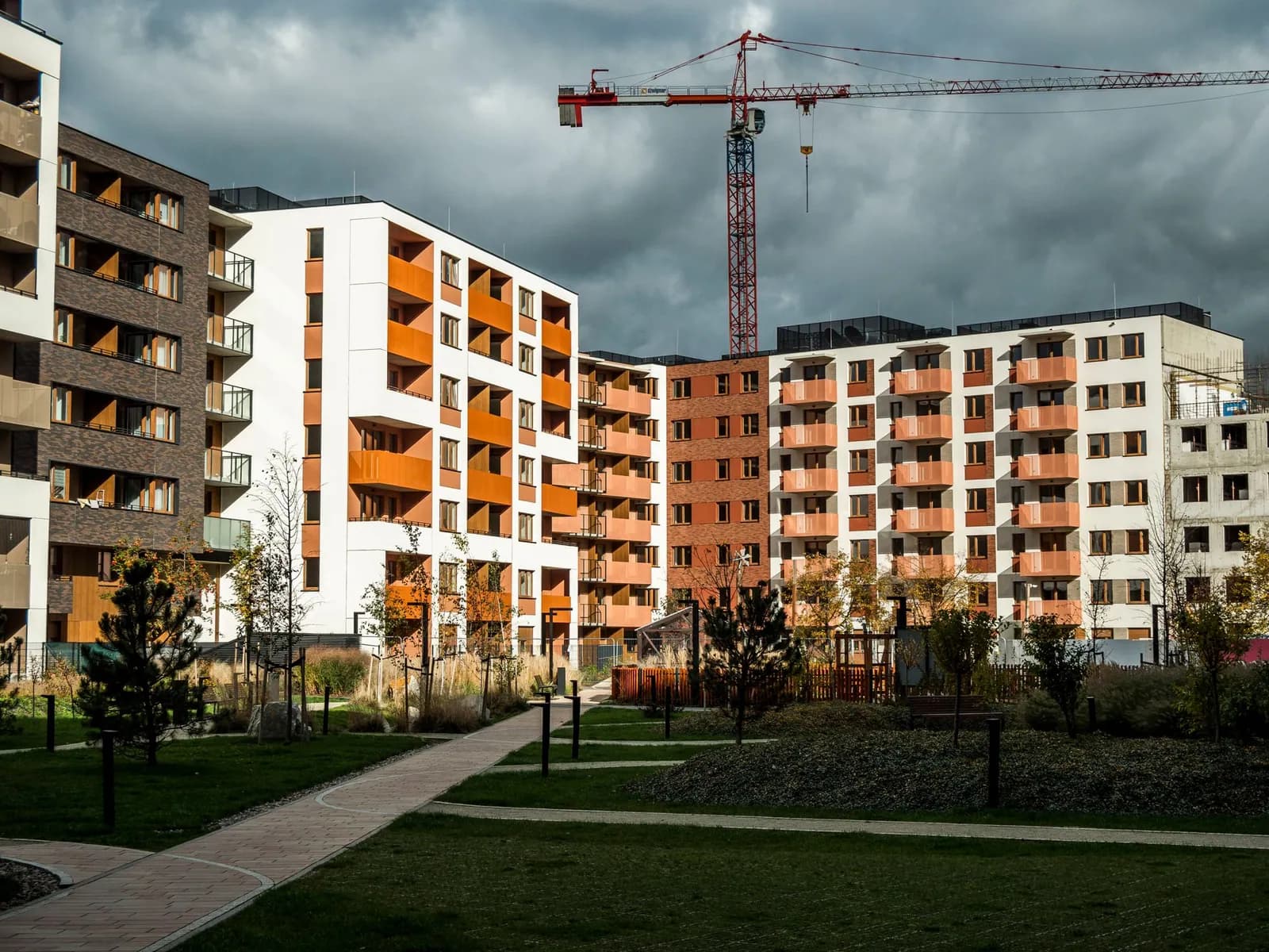 Neu gebaute Mehrfamilienhäuser mit Balkonen, dahinter ein Baukran vor dunklen Wolken