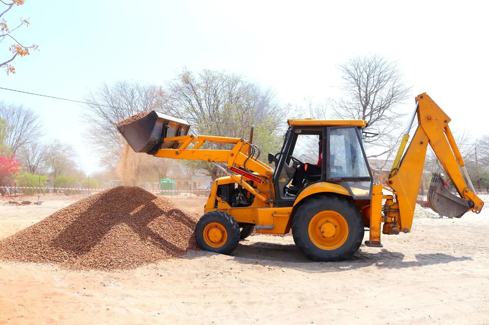 Gelber Baggerlader schüttet Kies mit der Frontschaufel auf einen Haufen auf einer sandigen Baustelle