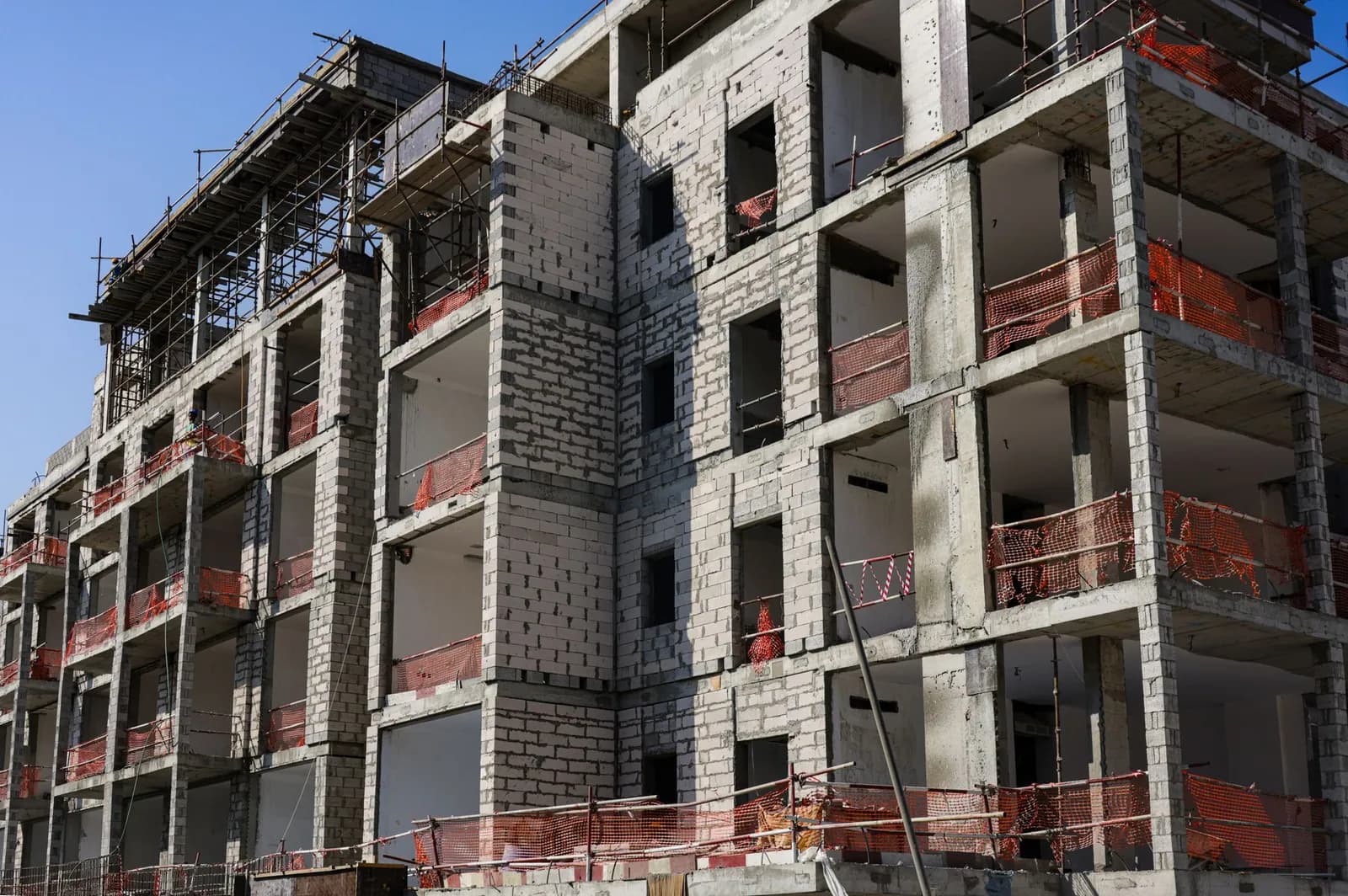 Rohbau eines mehrgeschossigen Wohnhauses mit Gerüst und orangefarbenen Schutznetzen