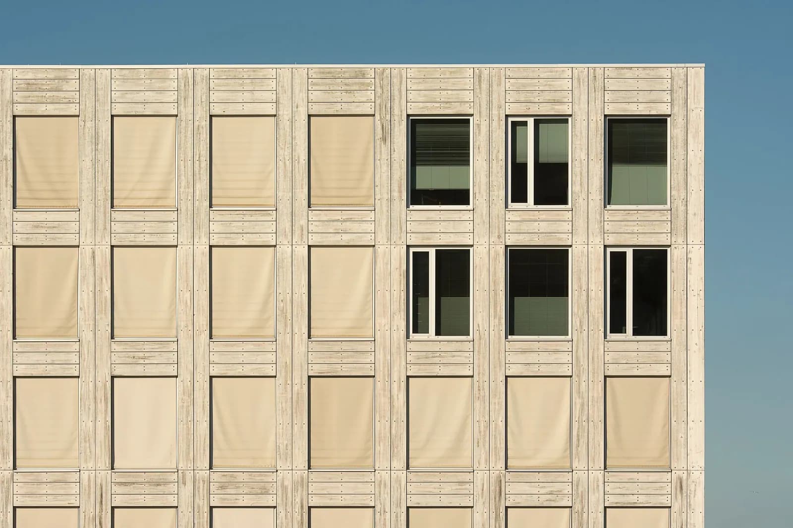 Zeitgenössische Holzfassade eines Gebäudes mit gleichmäßigem Fensterraster vor klarem Himmel