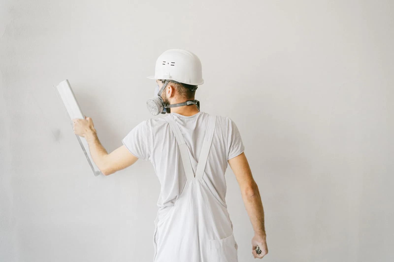 Handwerker in Schutzkleidung trägt mit der Kelle Putz auf eine weiße Wand auf