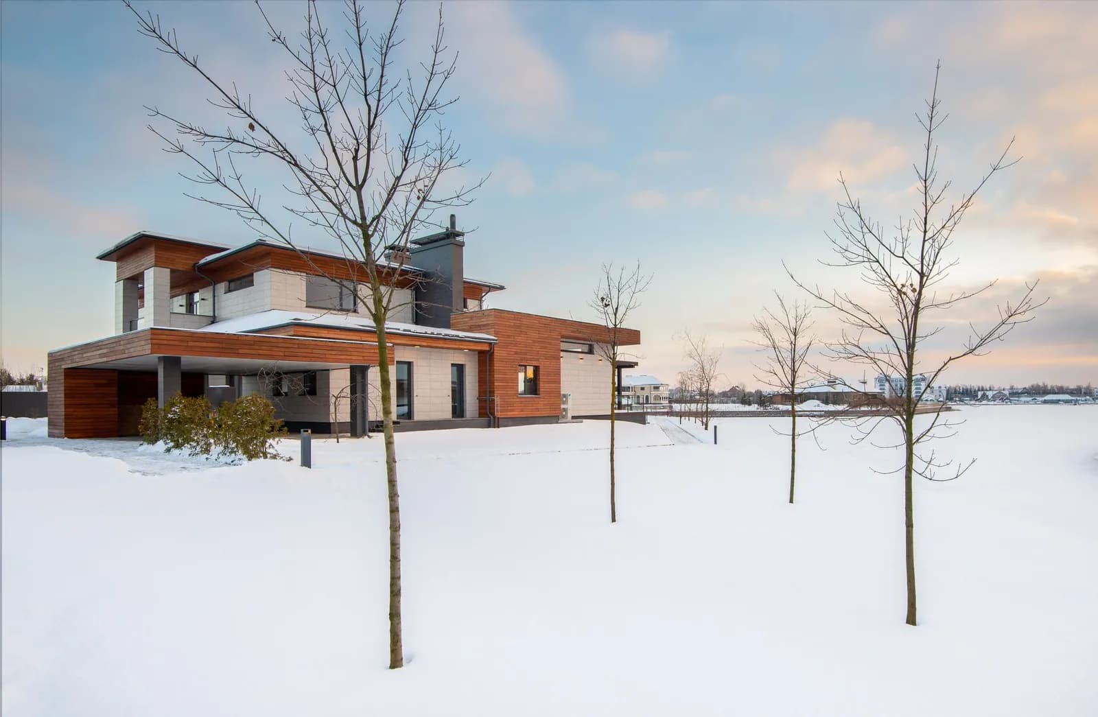 Zweigeschossiges Einfamilienhaus mit Stein- und Holzfassade im verschneiten Garten an einem Wintertag