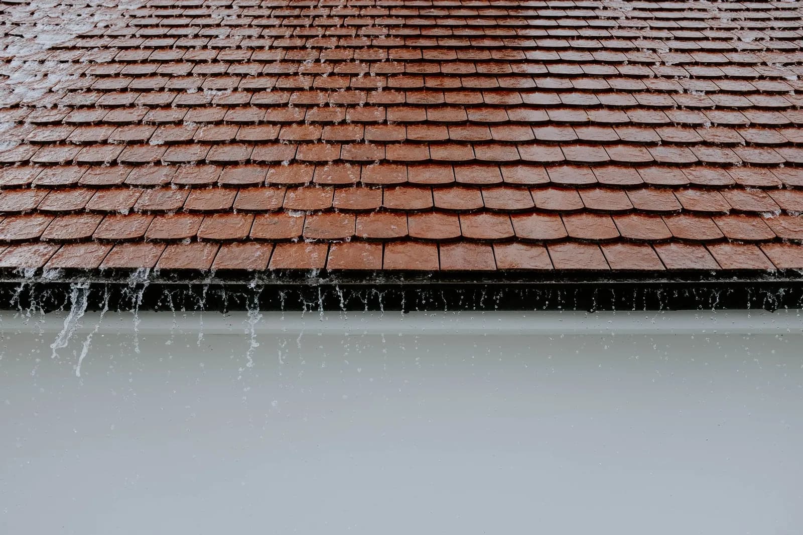Regenwasser läuft über braune Dachziegel bei Regen