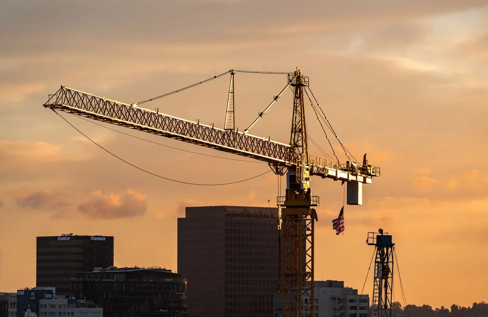 Baukran als Silhouette vor orangefarbenem Abendhimmel über Gebäuden einer Stadt