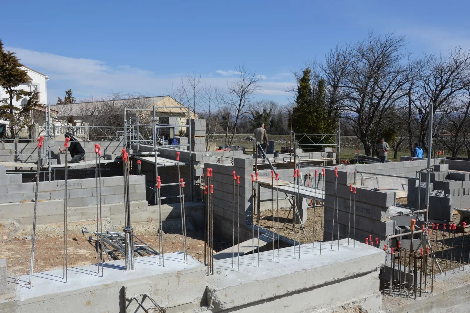Baustelle eines Wohnhauses mit Betonfundament, gemauerten Wänden und herausragenden Bewehrungsstäben